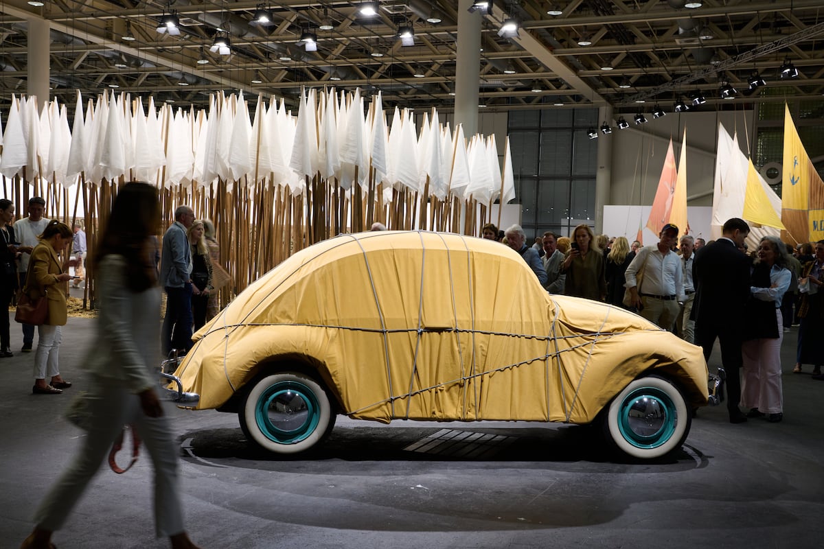 "'Volkswagen Beetle Saloon envolto' (1961) de Christo, e ao fundo, as bandeiras brancas de 'Progetto per la pace' (1968), de Mario Ceroli, na seção Unlimited da Art Basel. (Foto: Art Basel)"