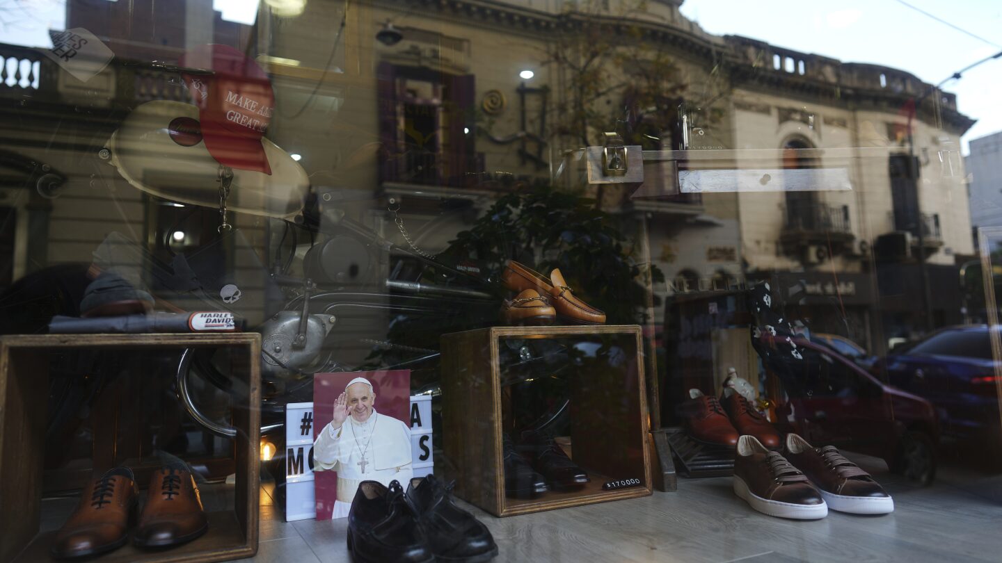Uma fotografia do falecido Papa Francisco está na janela da loja de sapatos Muglia, ao lado do modelo de sapatos que Jorge Bergoglio usou no bairro Flores, onde cresceu em Buenos Aires, Argentina, na quinta-feira, 24 de abril de 2025. (Foto: AP Photo/Natacha Pisarenko)