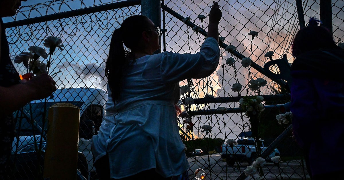 Pessoas colocam flores de cravo branco na cerca do Centro de Detenção Krome durante uma vigília em protesto contra a custódia e as deportações em massa do Serviço de Imigração e Alfândega dos EUA em Miami, em 24 de maio de 2025. (Foto: Giorgio Viera/AFP)