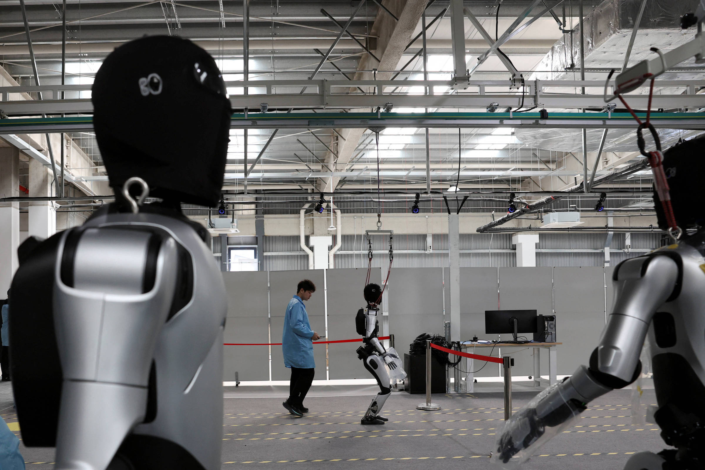 Um robô humanoide caminha enquanto funcionários realizam testes nos robôs, na linha de produção da fábrica da AgiBot em Xangai, China (Foto: Florence Lo/REUTERS)