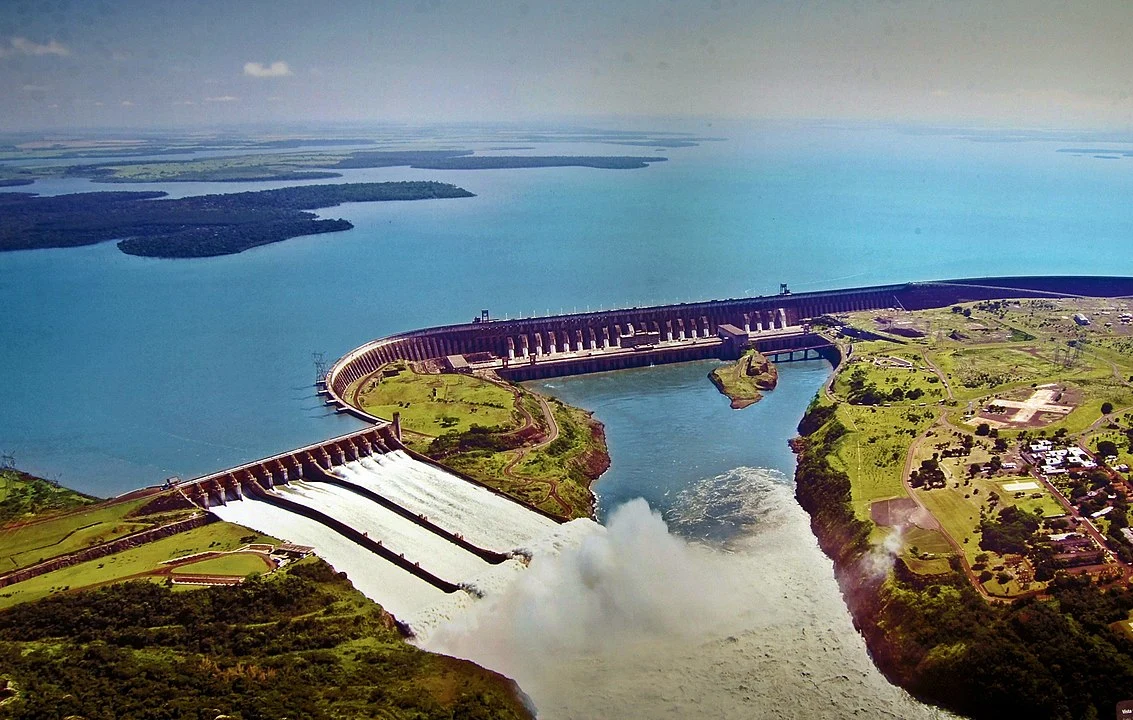 Foto de um lago em um dia ensolarado, com uma pessoa vestindo uma camiseta preta com um motivo de peixe e olhando para a câmera. (Foto: Reprodução)