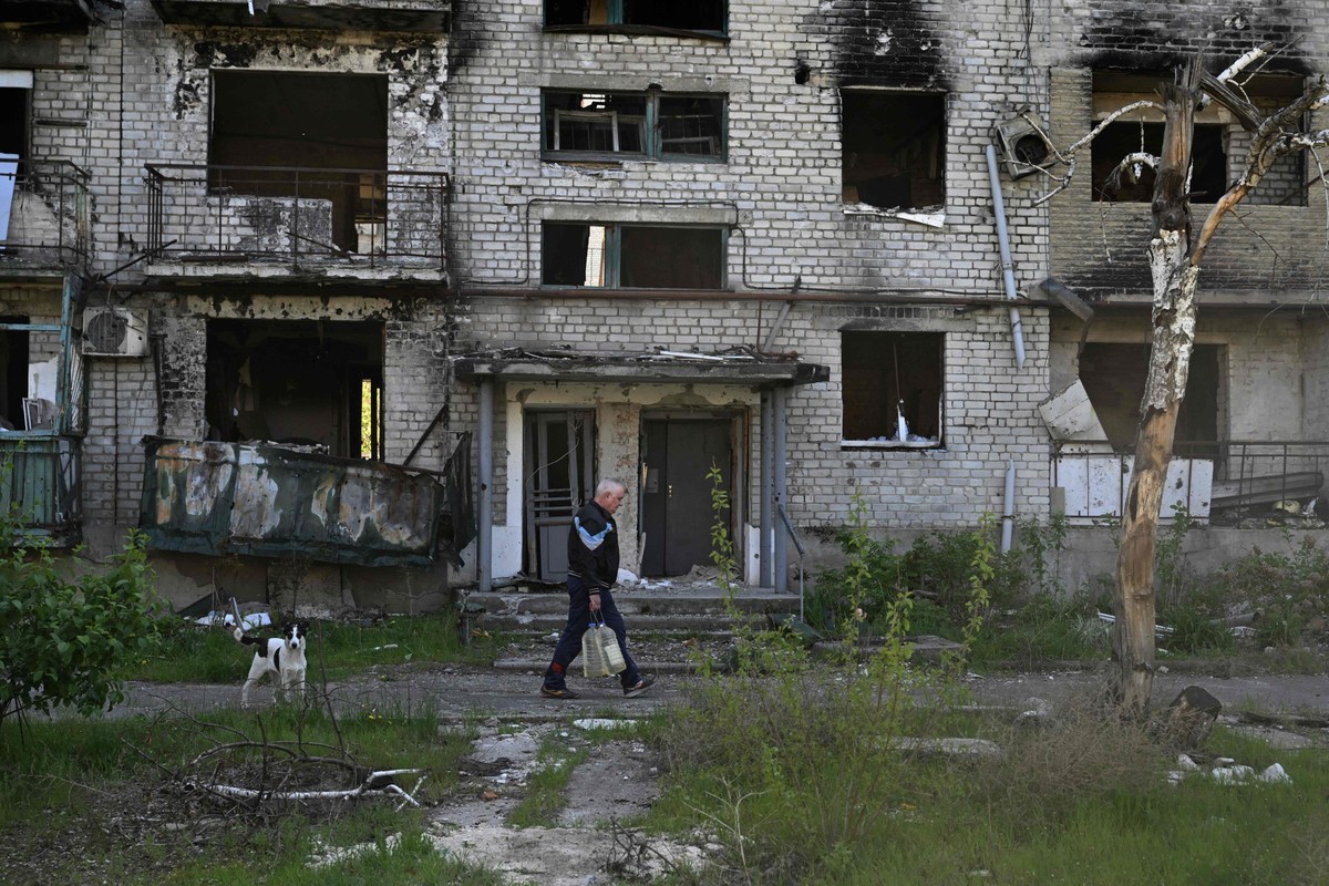 Morador caminha junto a um prédio bombardeado na cidade de Lyman, na Ucrânia (Foto: Genya SAVILOV / AFP)