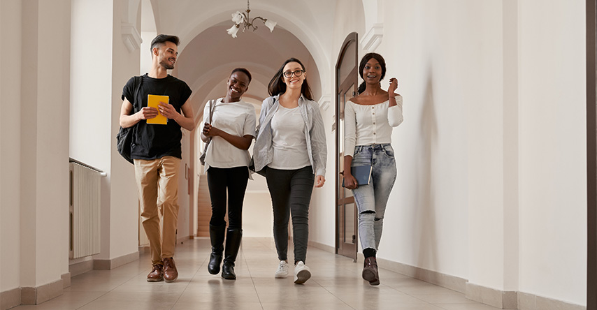 Grupo de 4 jovens caminhando pelo corredor com seus materiais escolares.