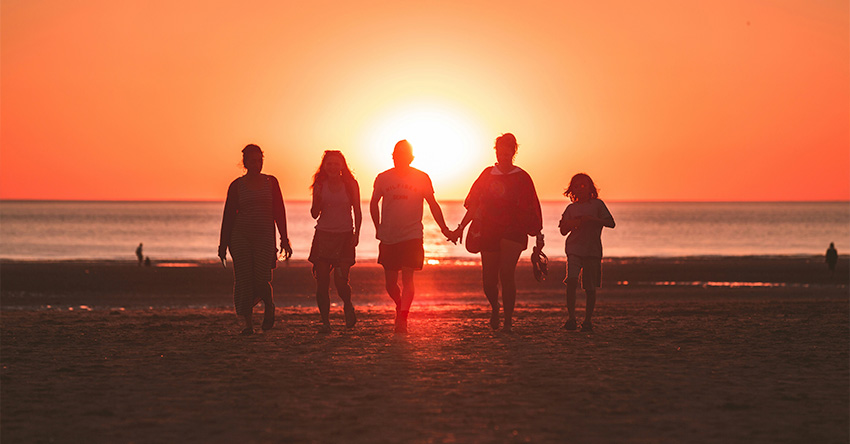 Familia caminhando em direção oposta ao do sol em uma praia.