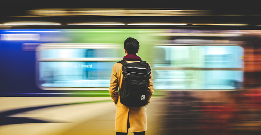 Homem em uma estação de trem, atrás do trem em movimento.