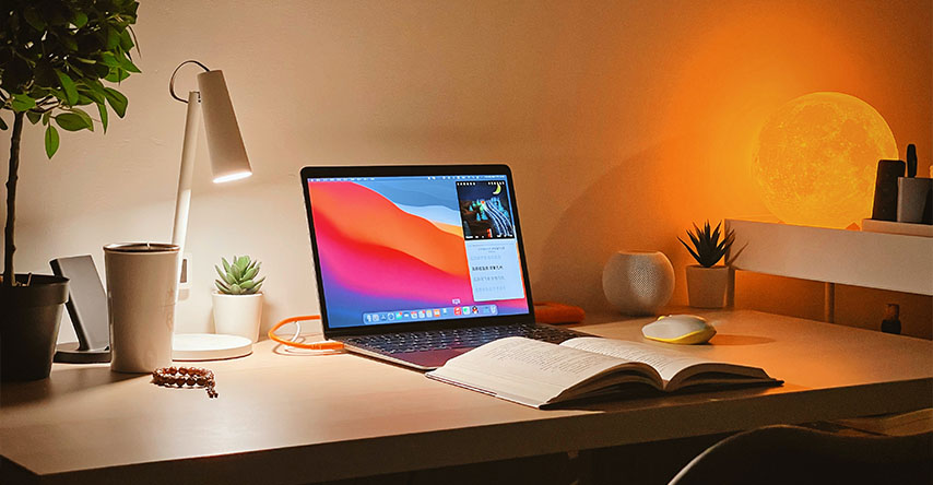 Foto de uma área de estudos, com um livro, computador, luminárias e outras decorações.