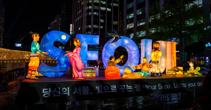 Letreiro na cidade de Seoul, com o nome da cidade e alguns bonecos asiáticos em volta.