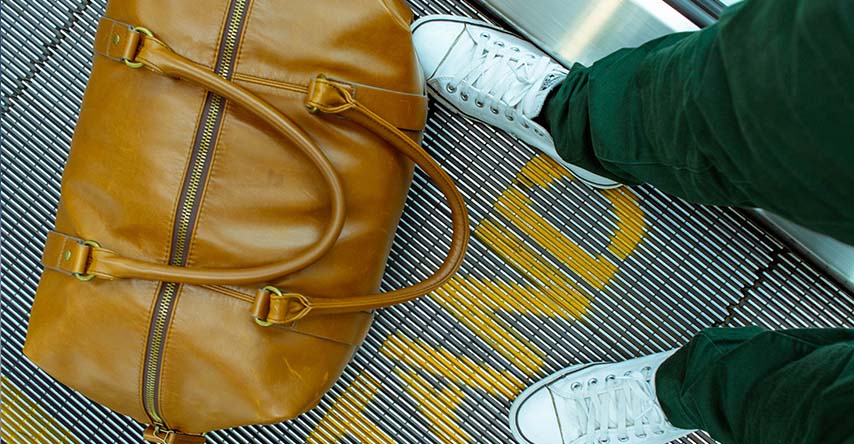 Imagem de cima, mostrando uma mala fechada aos pés de uma pessoa