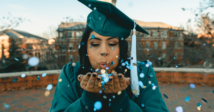 pessoa com chapéu de graduação soprando confetes