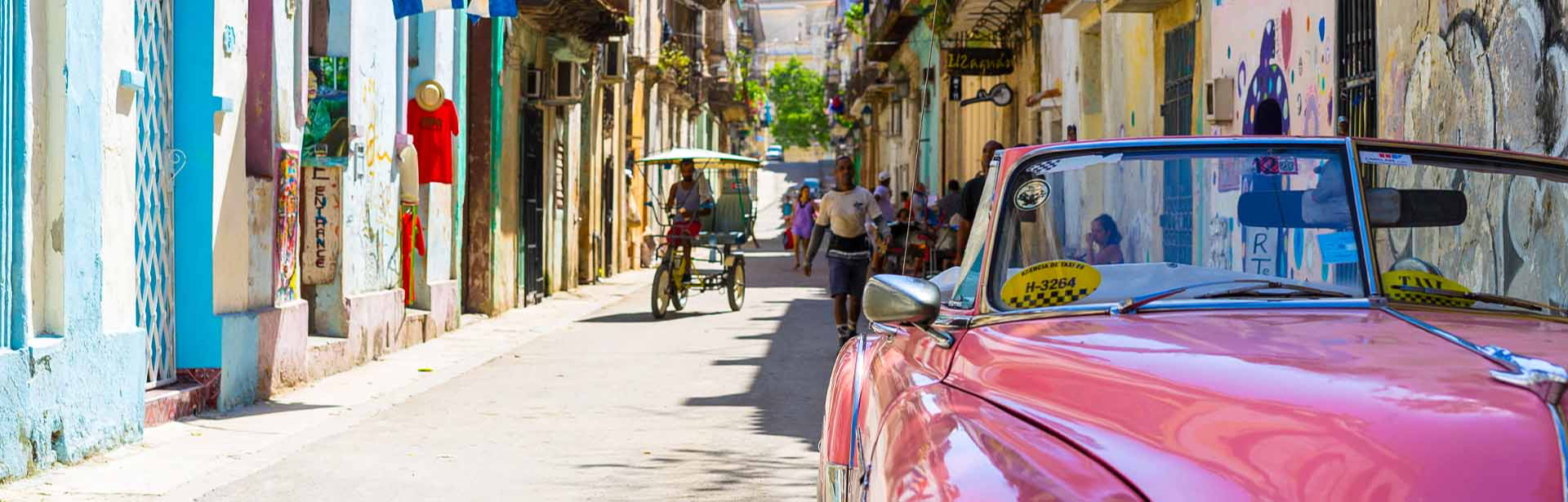 Carro rosa estacionado em um rua de Cuba, com pessoas andando atrás dele
