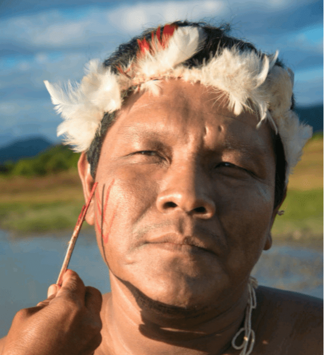 Na imagem, aparece Enoque Raposo usando ornamentos Maxui e pintando o rosto com grafismos em vermelho.