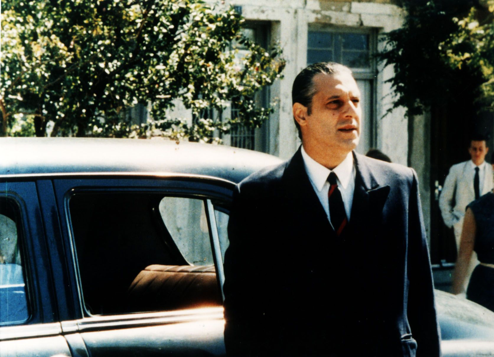 Ant&ocirc;nio Fagundes est&aacute; em frente a um carro. Ele usa camisa branca, terno e gravata pretos.