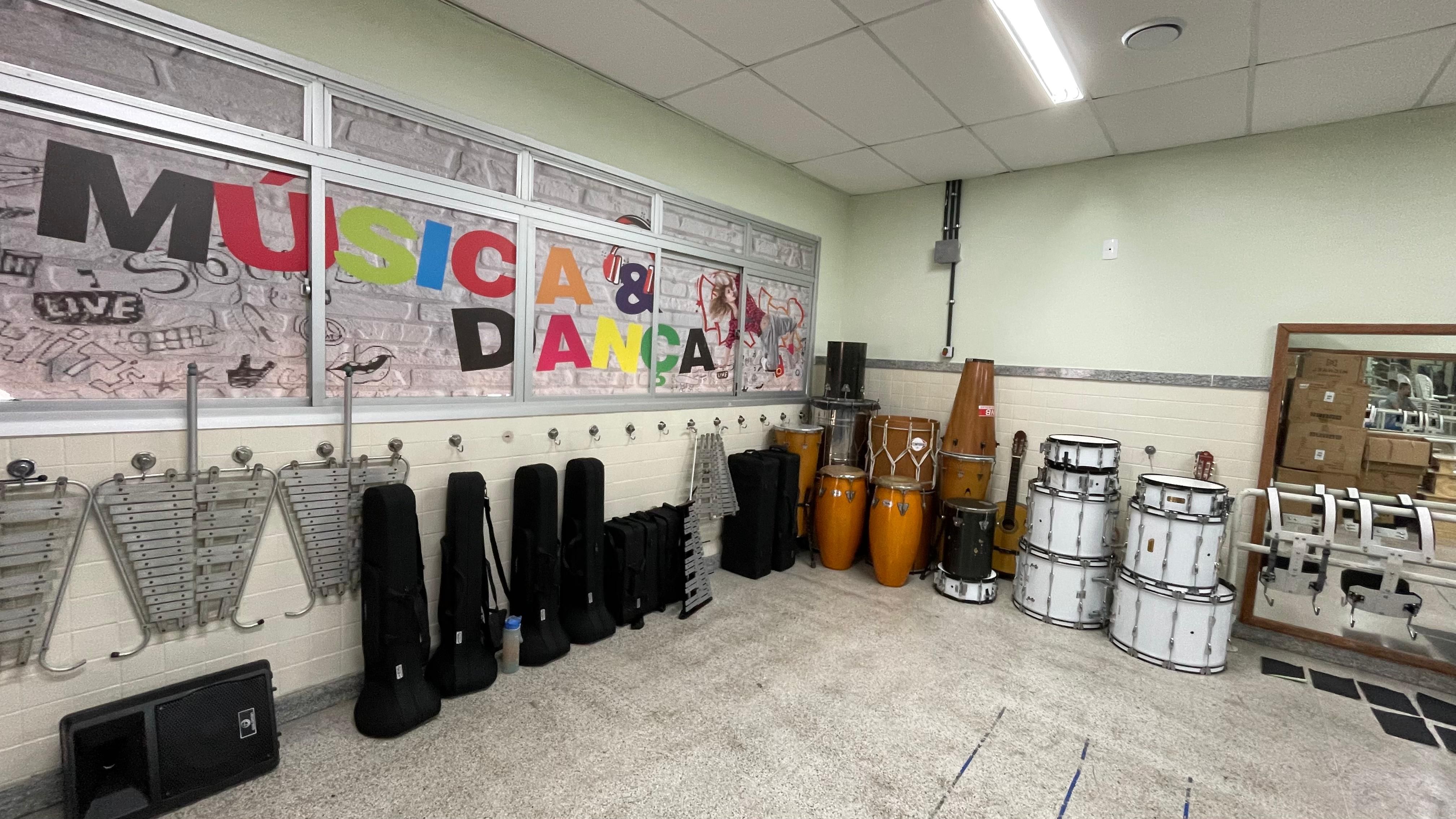 Foto de um amplo canto de uma sala de m&uacute;sica. Na parede da esquerda, uma janela de vidro exibe um adesivo colorido com a frase 