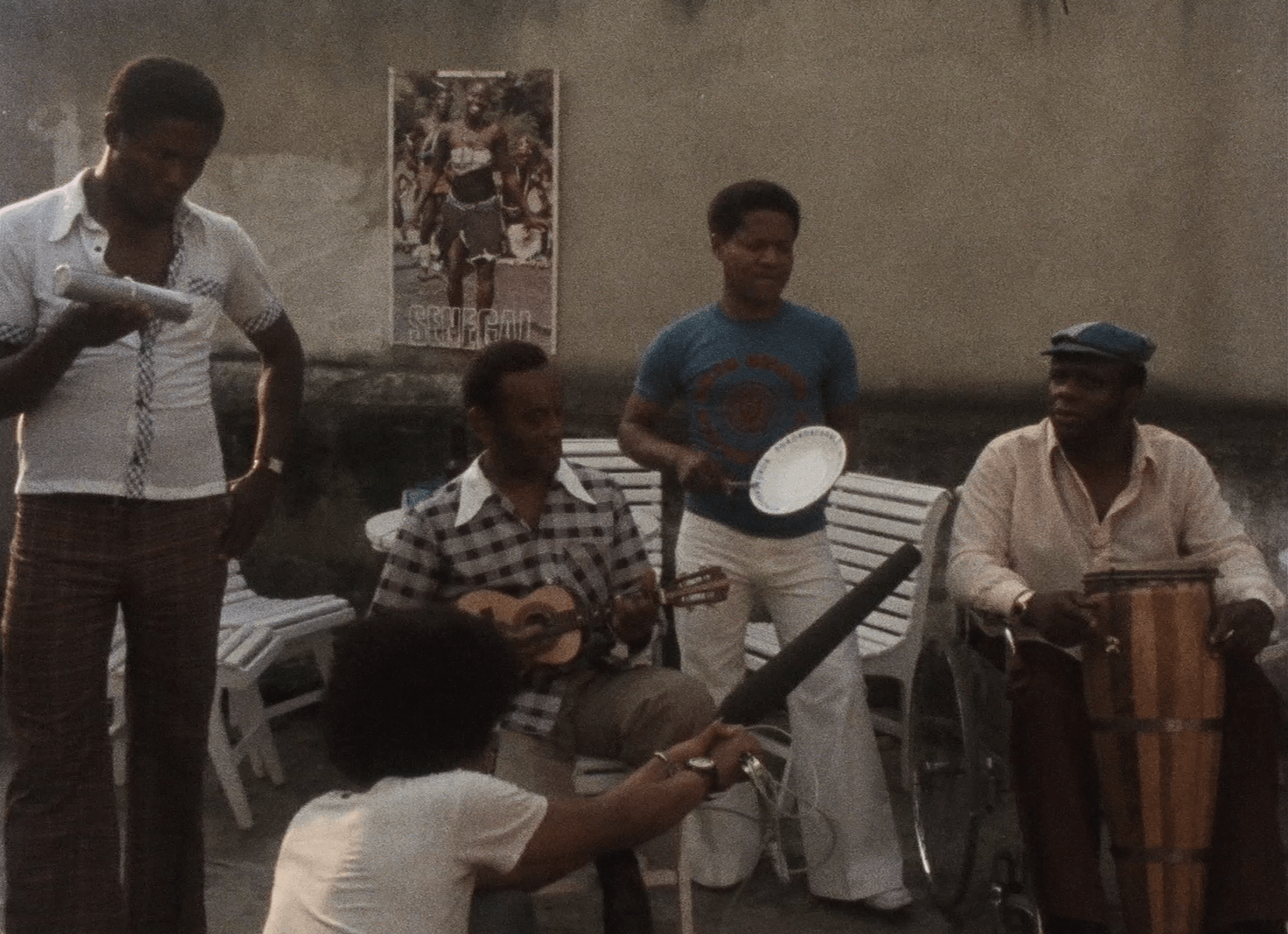 Uma roda de samba, com m&uacute;sicos tocando diversos instrumentos, como prato e cavaquinho. Todos os artistas que est&atilde;o na imagem s&atilde;o homens negros.
