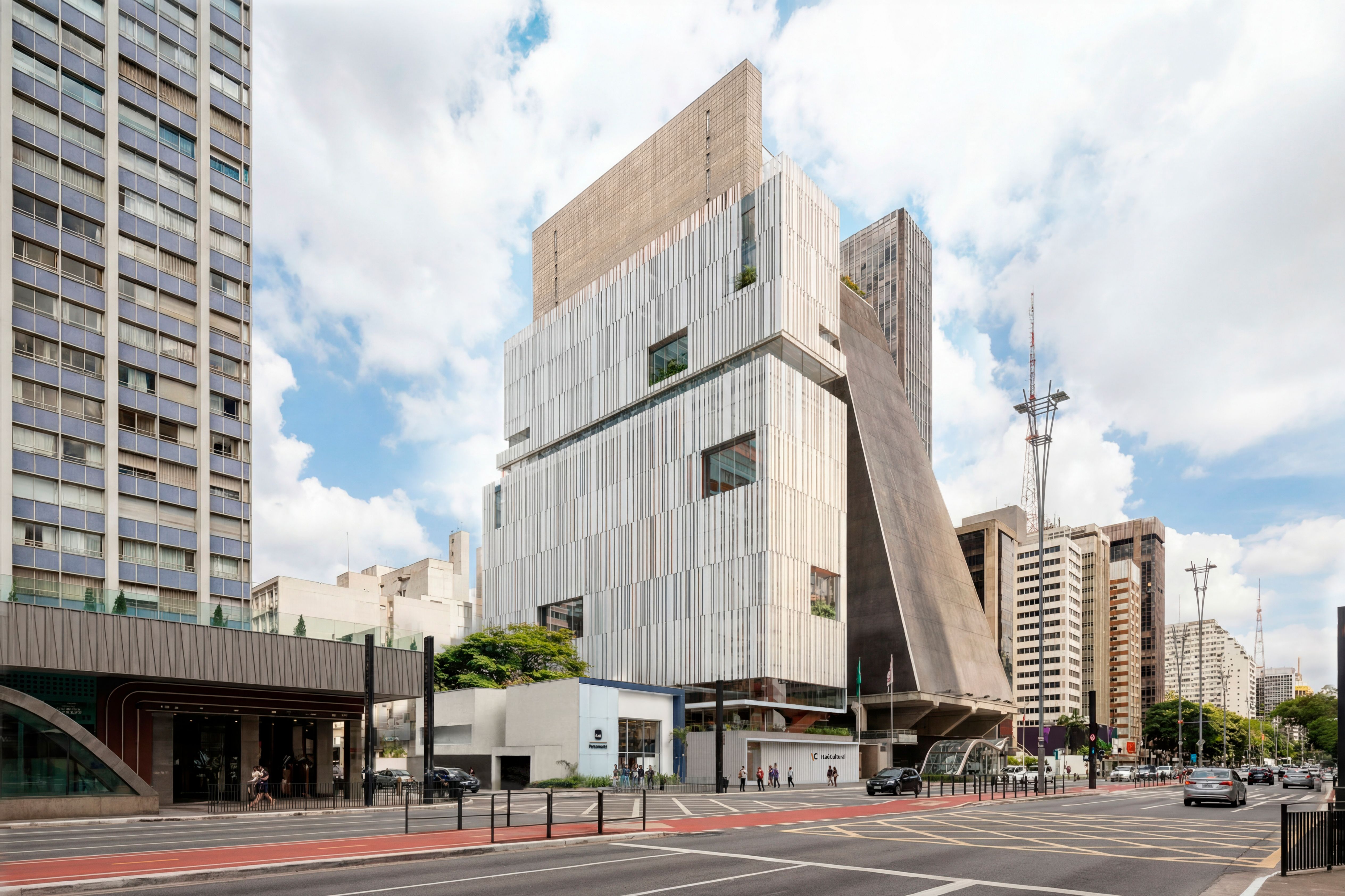 Simulação da nova fachada do Itaú Cultural. Em destaque, o edifício tem feição moderna e apresenta ripas verticais brancas e aberturas quadradas. Ao lado, a estrutura piramidal do prédio da Fiesp. Em frente, a avenida movimentada com ciclovia vermelha, carros e pedestres sob um céu claro. Simulação da nova fachada do Itaú Cultural. Em destaque, o edifício tem feição moderna e apresenta ripas verticais brancas e aberturas quadradas. Ao lado, a estrutura piramidal do prédio da Fiesp. Em frente, a avenida movimentada com ciclovia vermelha, carros e pedestres sob um céu claro.
