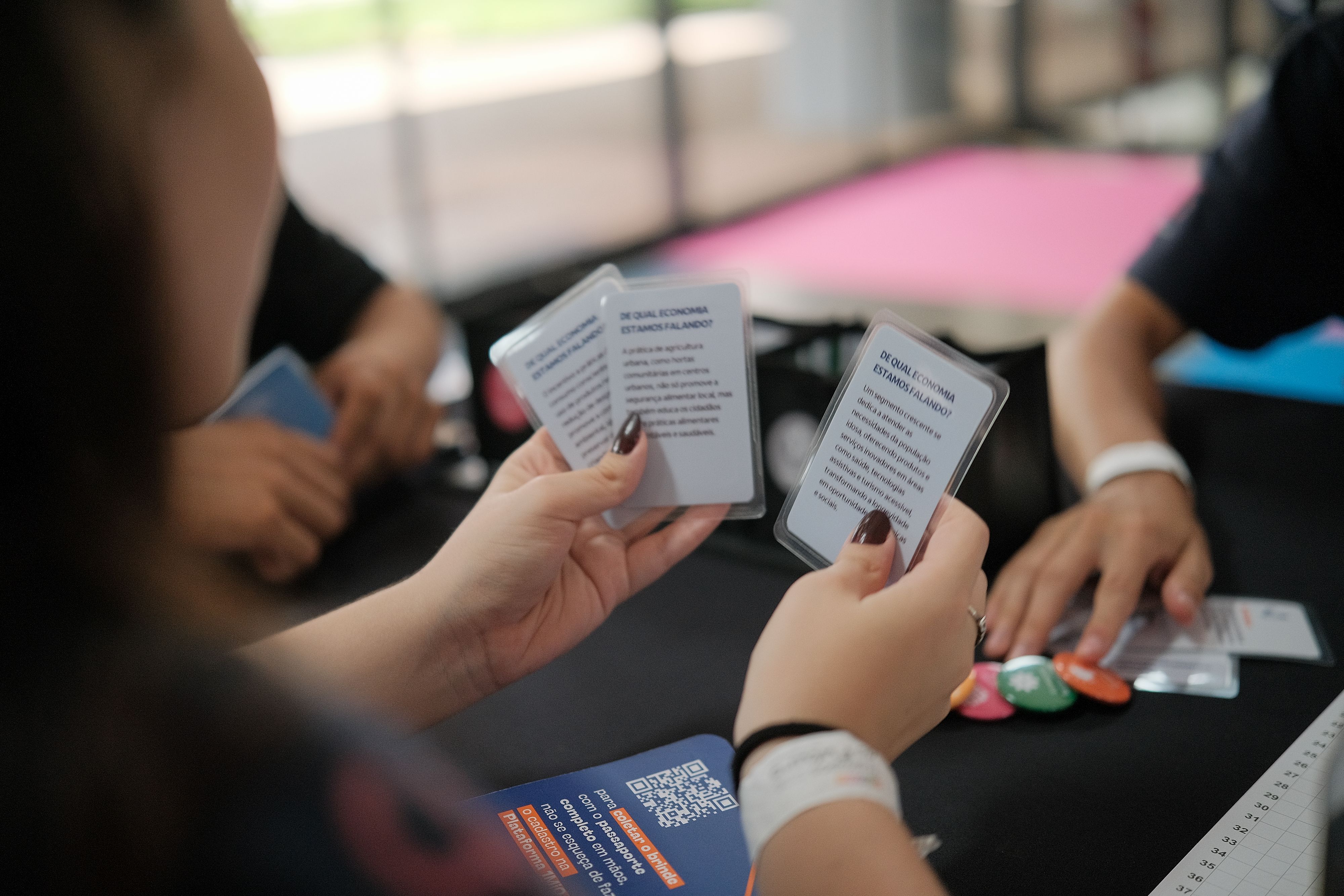 Podemos visualizar uma participante do jogo segurando tr&ecirc;s cartas referentes a din&acirc;mica do Jogo Trampos do Futuro.