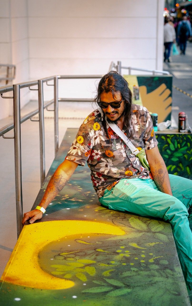 Sentado em um banco de cimento, André Mogle observa sua pintura na estrutura, um sol bem amarelo.