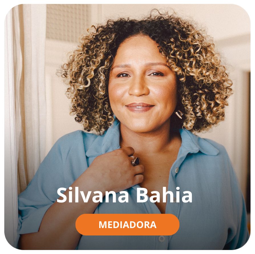 Uma mulher negra, de cabelos cacheados na altura dos ombros, na cor preta com alguamas mechas loiras. Ela veste uma camisa azul e est&aacute; sorrindo olhando em dire&ccedil;&atilde;o &agrave; c&acirc;mera 