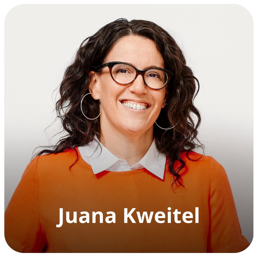 Uma mulher branca, de cabelos pretos, ondulados, na altura dos ombros. Ela usa &oacute;culos, veste uma camisa branca com uma camiseta em sobreposi&ccedil;&atilde;o laranja. Ela est&aacute; sorrindo em dire&ccedil;&atilde;o &agrave; c&acirc;mera 