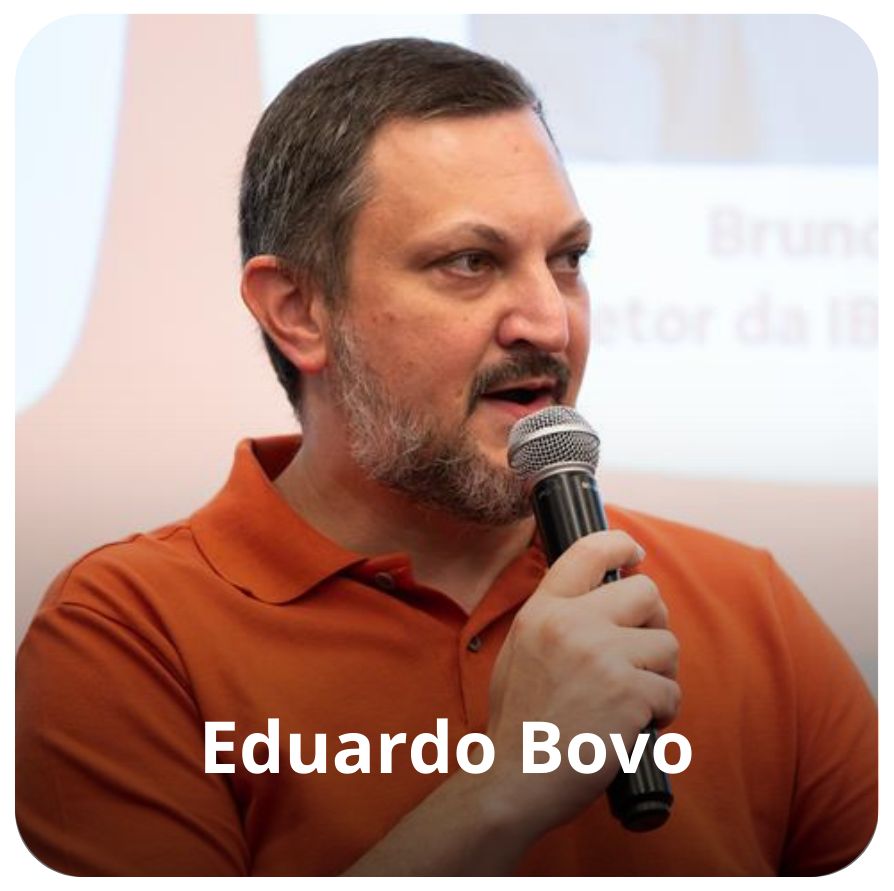 Eduardo Bovo &eacute; um homem branco, de cabelo curto e barba grisalha. Ele veste uma camiseta laranja e est&aacute; segurando um microfone enquanto fala olhando em dire&ccedil;&atilde;o ao p&uacute;blico. 