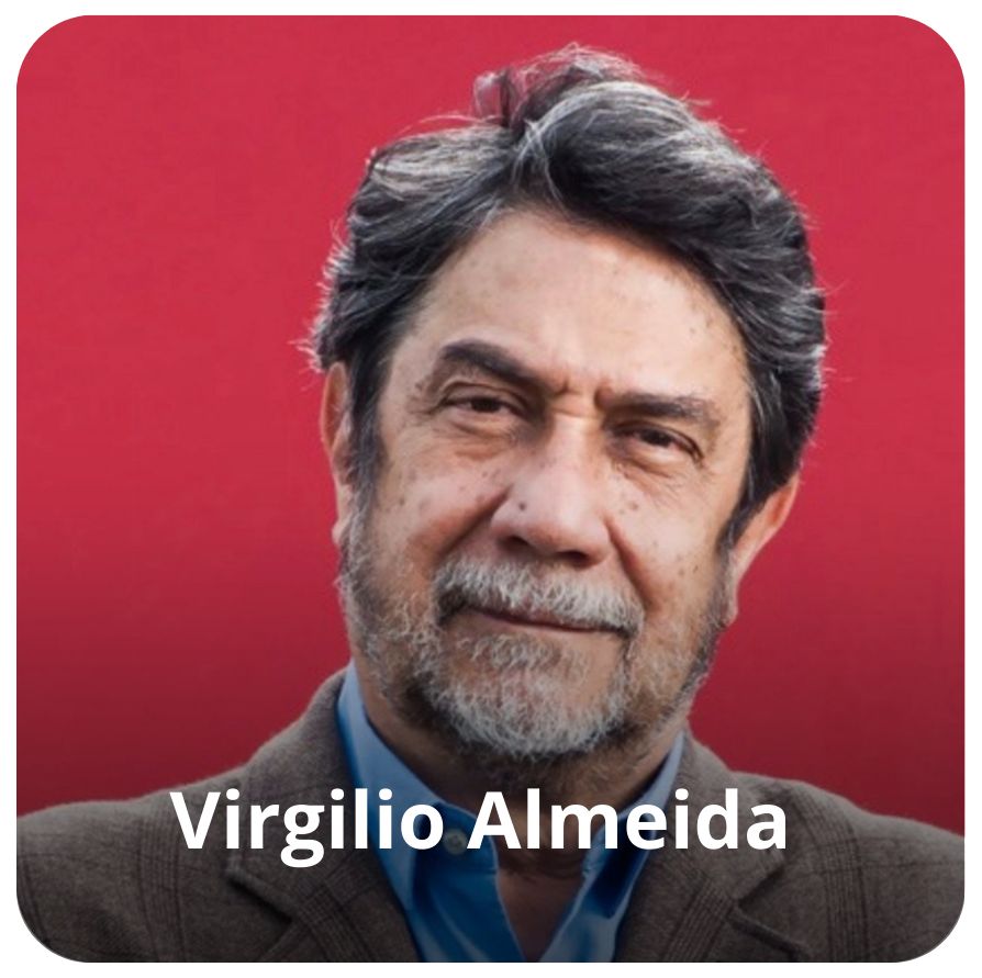 Um homem branco, de cabelos curtos e barba grisalhaos. Ele veste uma camisa azul e um palet&oacute; marrom 