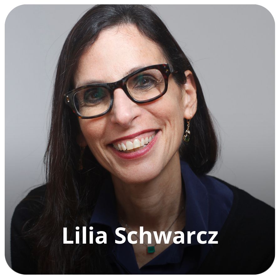 Uma mulher branca, de cabelos lisos, longos e preto. Ela usa &oacute;culos, brinco nas orelhas e veste uma camisa azul com um casaco preto.