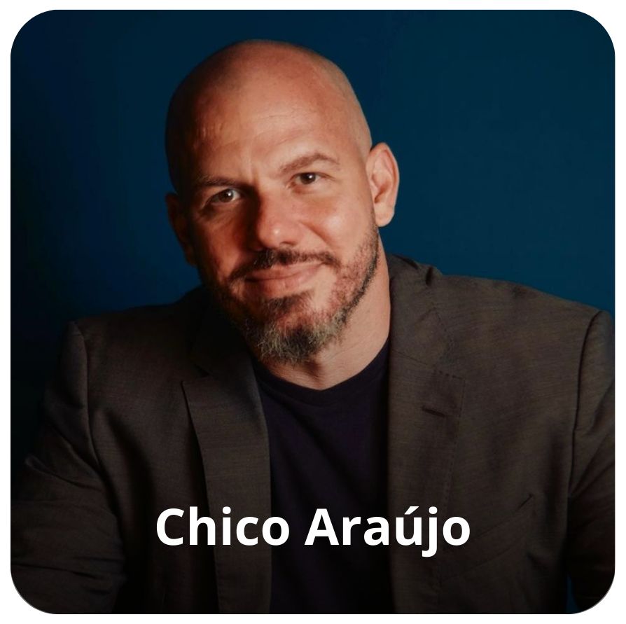 Um homem branco, sem cabelos e com uma barba grisalha. Ele veste uma camiseta azul escuro e um palet&oacute; cinza. 