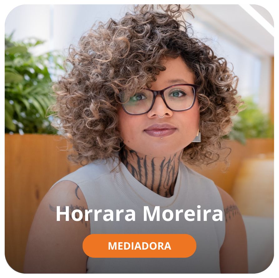 Uma mulher negra de pele clara, com cabelos cacheados preto com mechas brancas. Ela usa oculos e veste uma camiseta branca sem mangas e tem algumas tatuagens na regi&atilde;o do pesco&ccedil;o 