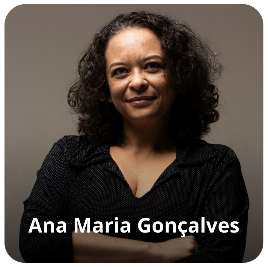 Uma mulher negra, de cabelos ondulados e pretos. Ela veste uma camisa preta com pontilhados em branco.