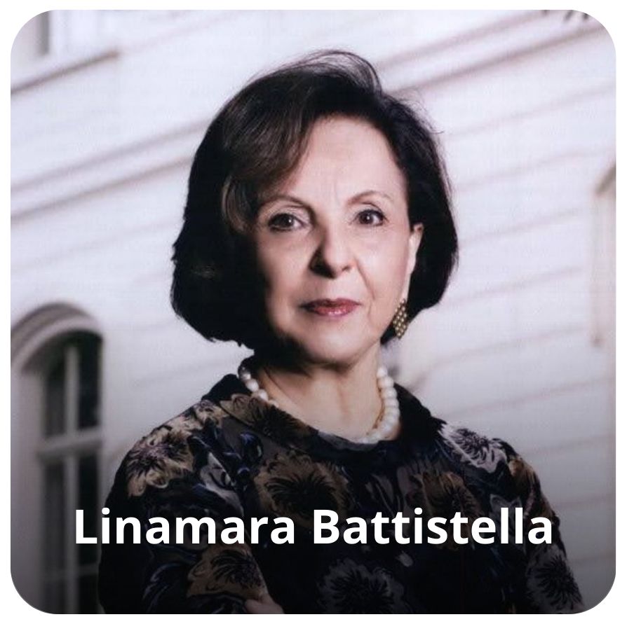 Uma mulher branca, de cabelos pretos abaixo da orelha. Ela veste uma blusa desenhadas com flores em tons de amarelo, branco e preto. Ela usa brincos nas orelhas e um colar de p&eacute;rola. 