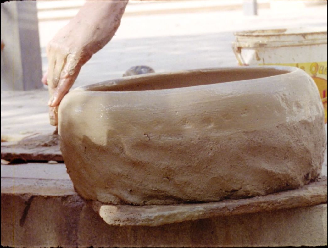 A imagem mostra uma mão trabalhando na feitura de um vaso de barro.