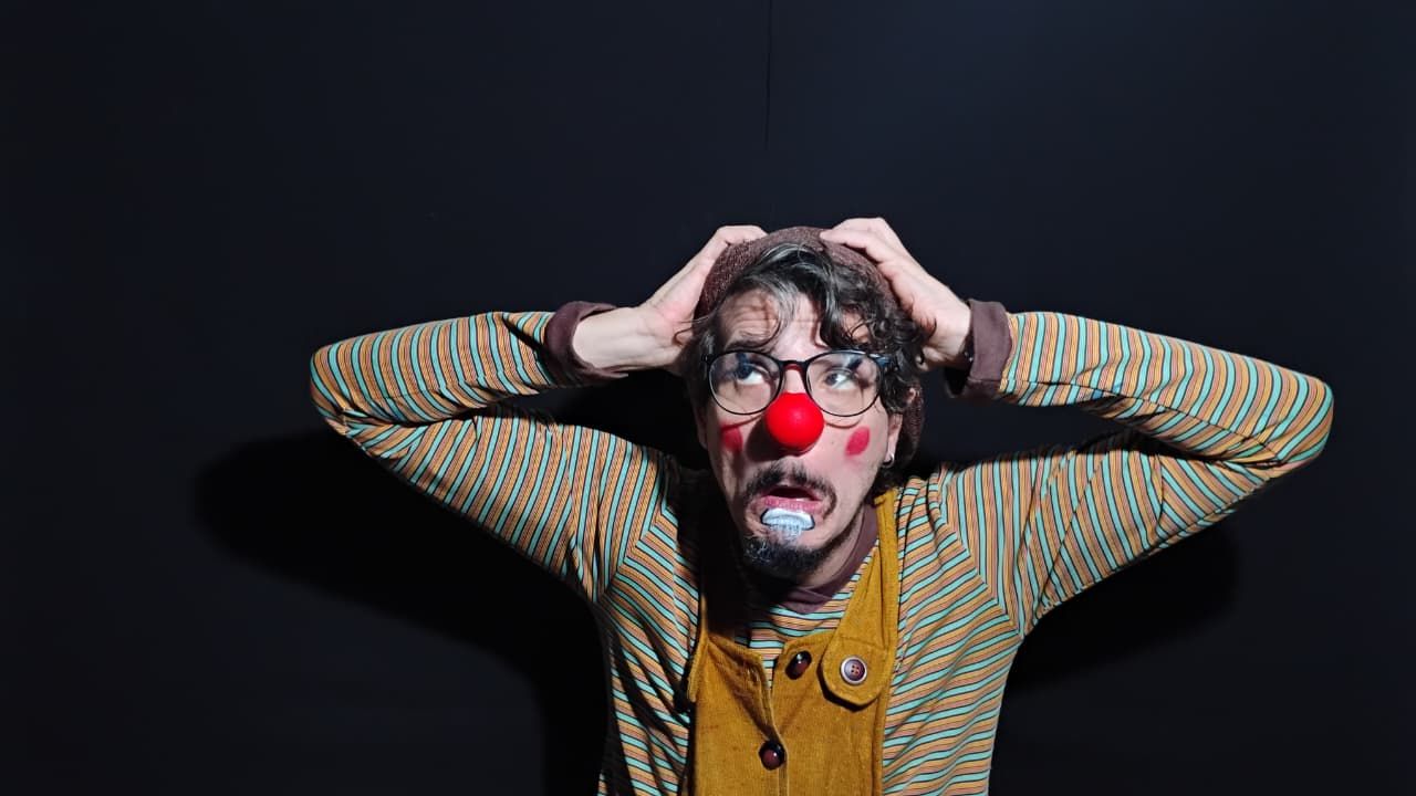 Igor Rocha aparece como o palhaço Surddy. Ele é um homem branco, veste uma blusa listrada e um macacão amarelo e está com as mãos na cabeça. O ator usa também uma boina marrom, óculos de grau e um nariz vermelho de palhaço.