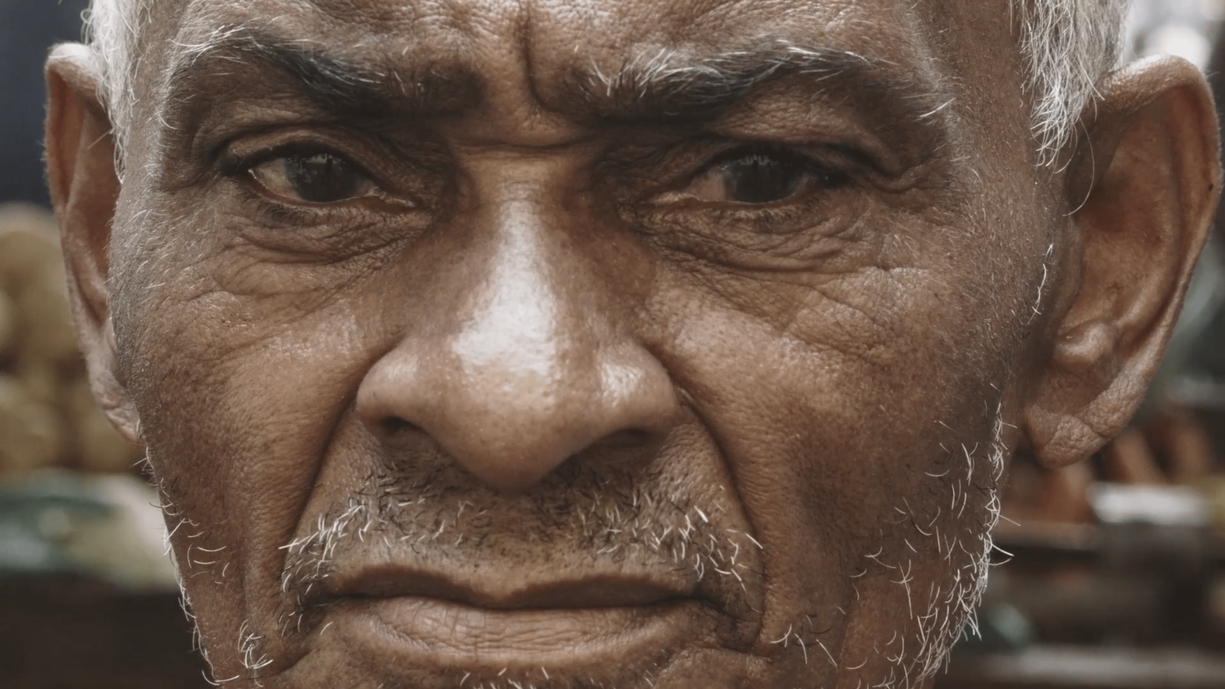 A imagem traz o rosto de um senhor negro. Ele tem o semblante sério e cabelos brancos.