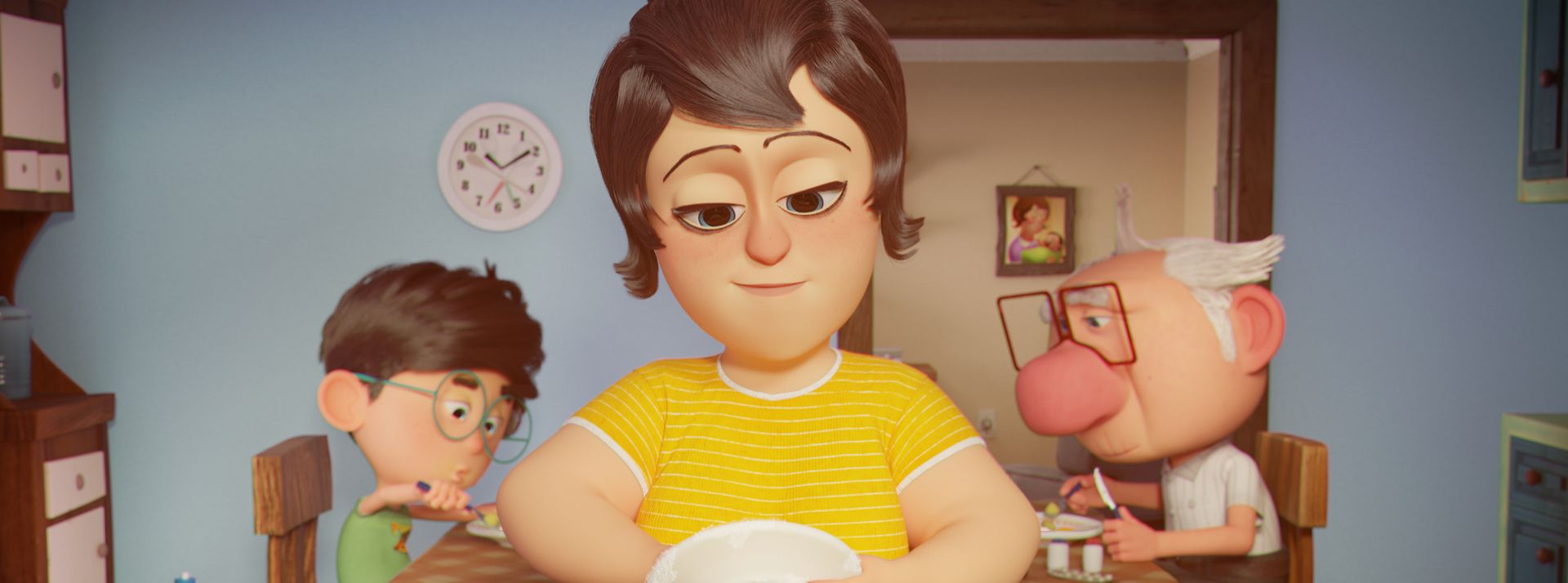 Na cozinha, a mãe está lavando louça. Ela é branca, usa uma blusa amarela e tem cabelo castanho. Atrás, na mesa, há o neto e o avô.